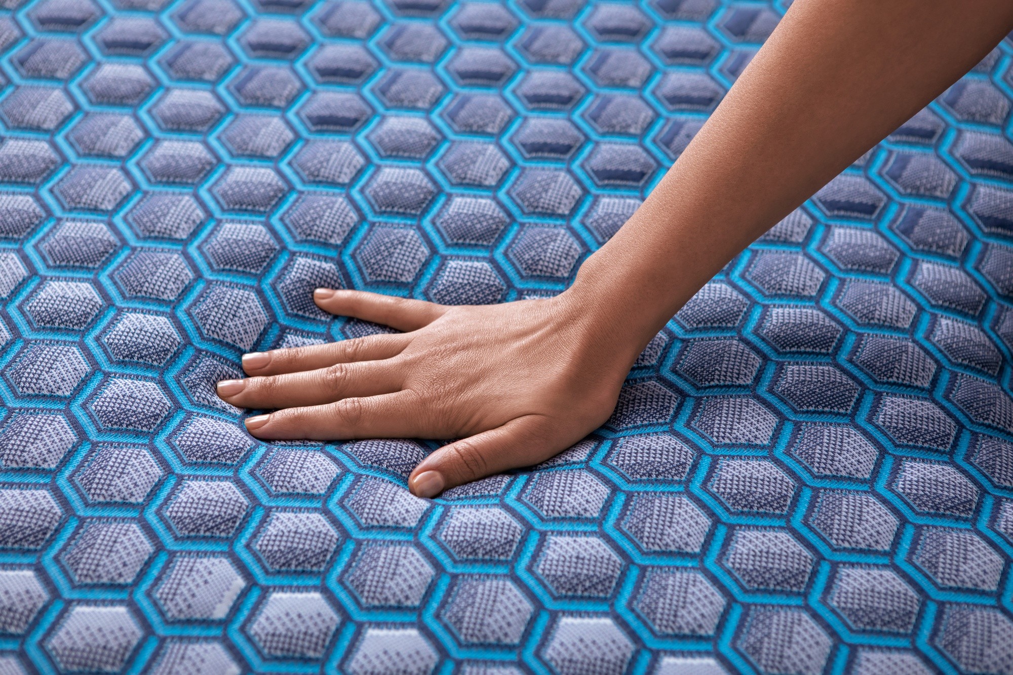 woman's hand pressing down on a blue Sealy FlexGrid mattress