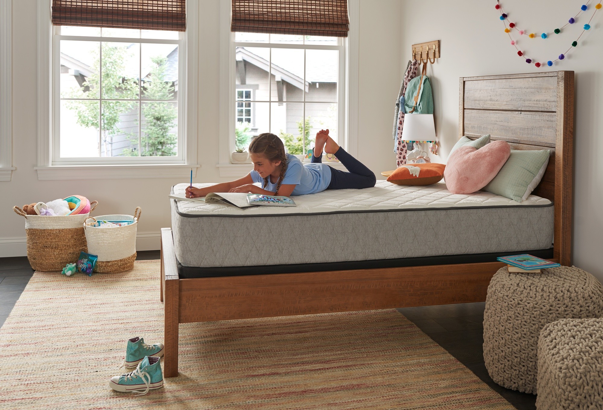 A young girl doing homework on a Sealy Essentials mattress.