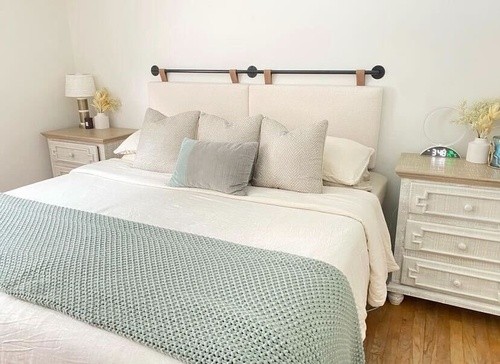 made bed with white and light teal bedding with cream headboard and white wooden side tables